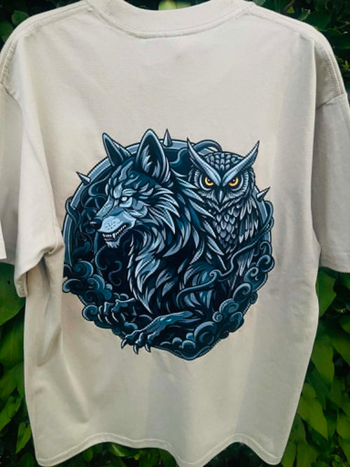 An light green short-sleeve t-shirt featuring a large graphic print of a blue wolf and owl in a circular design, set against a background of green foliage.